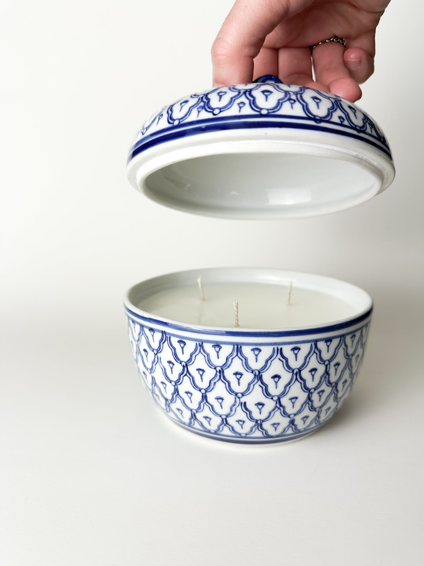 Ceramic container with blue geometric pattern being opened by a hand on a white background