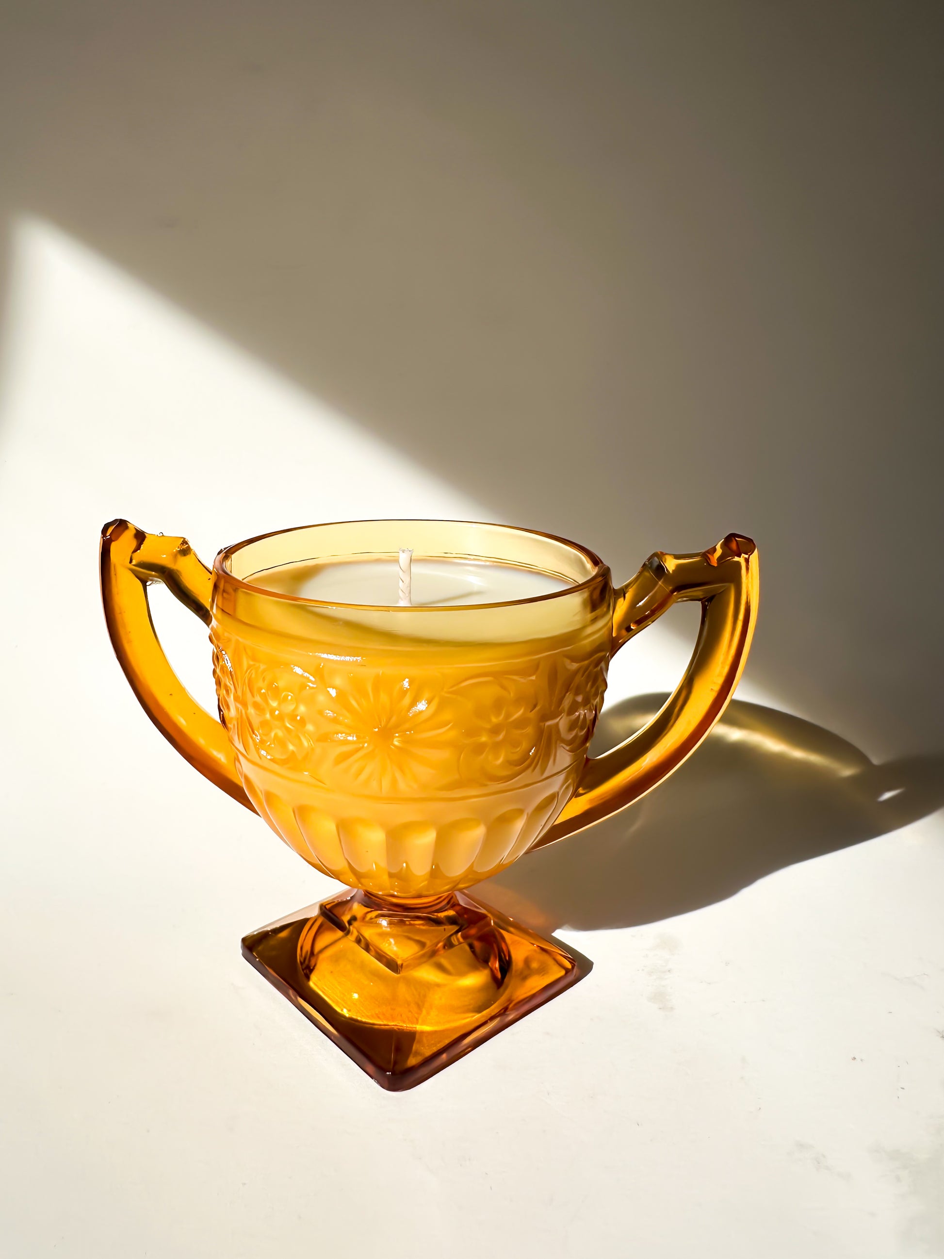 Amber glass candle holder with a candle inside on a white surface.