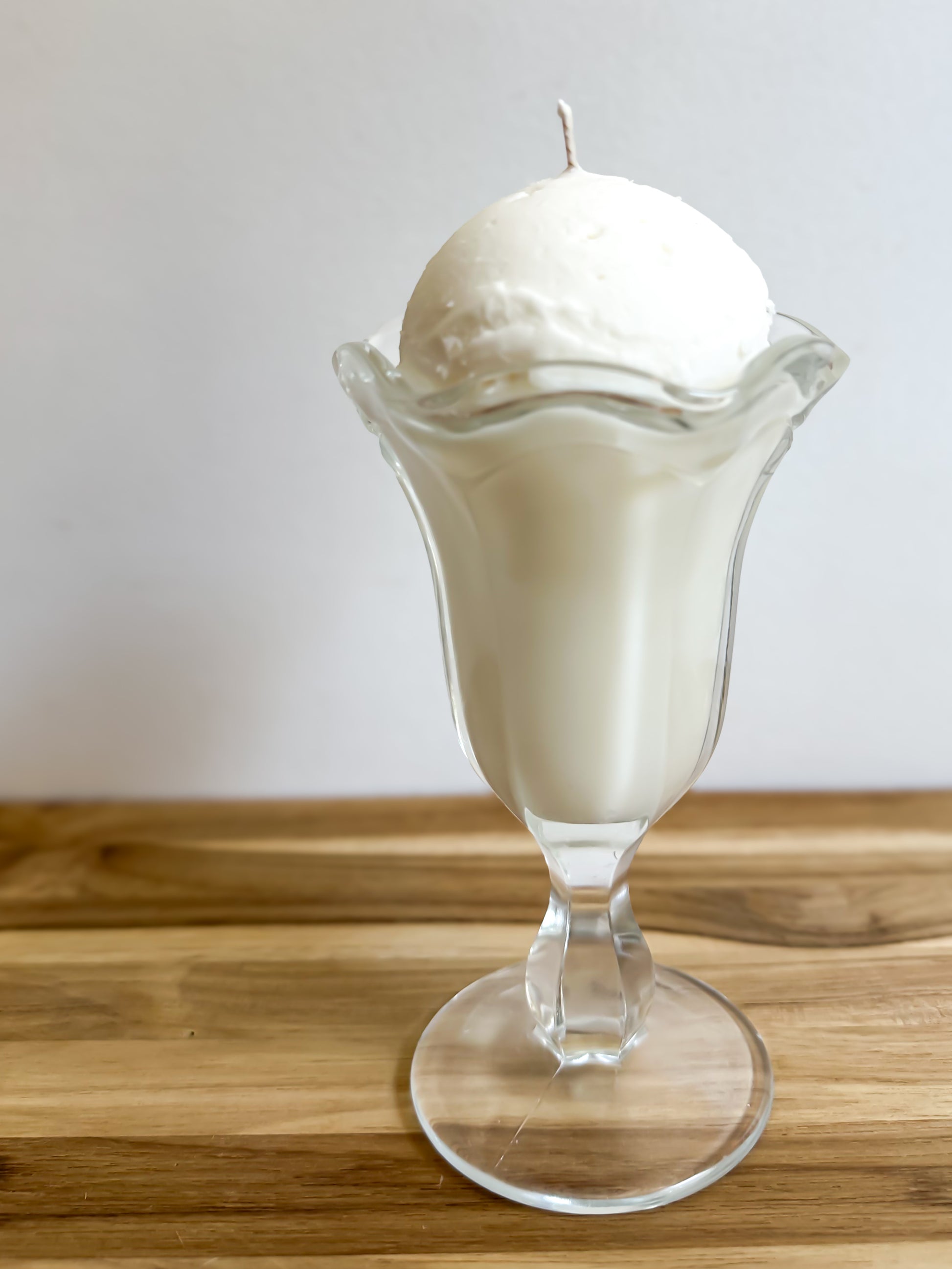 Glass ice cream sundae with a scoop of vanilla ice cream on a wooden surface.