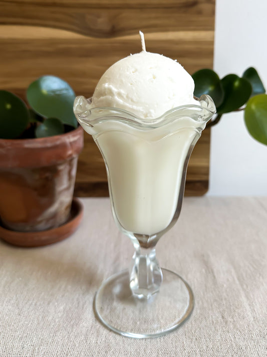Candle in a glass ice cream bowl with plants in the background