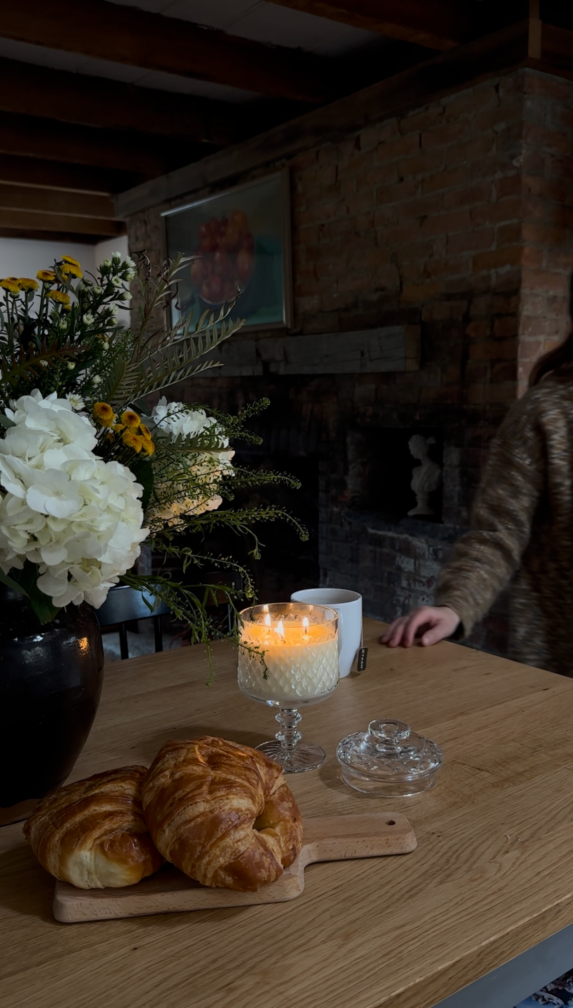 Table with croissants, a candle, and flowers in a cozy indoor setting.