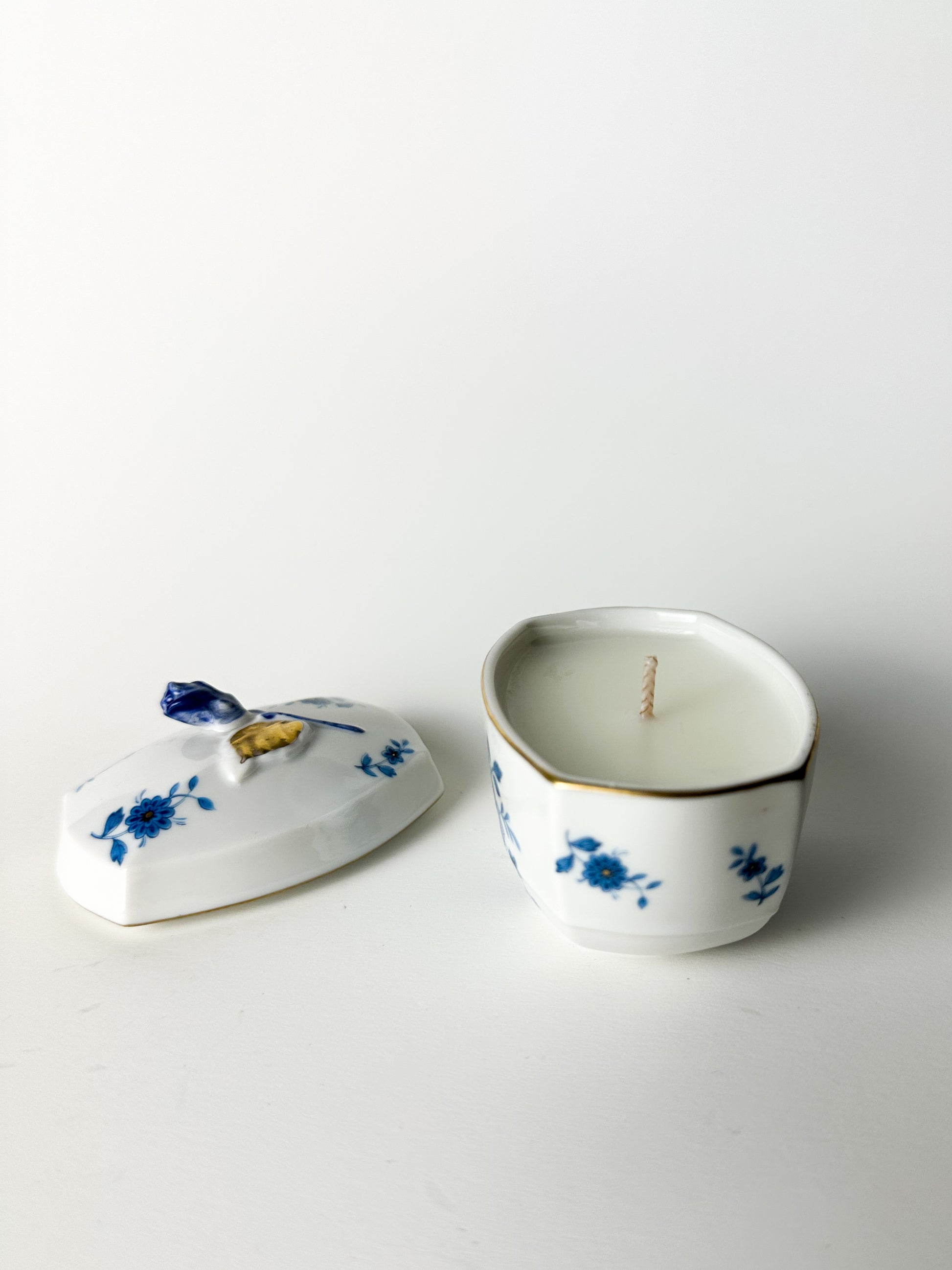 Ceramic container with floral design on lid and body, containing a candle.