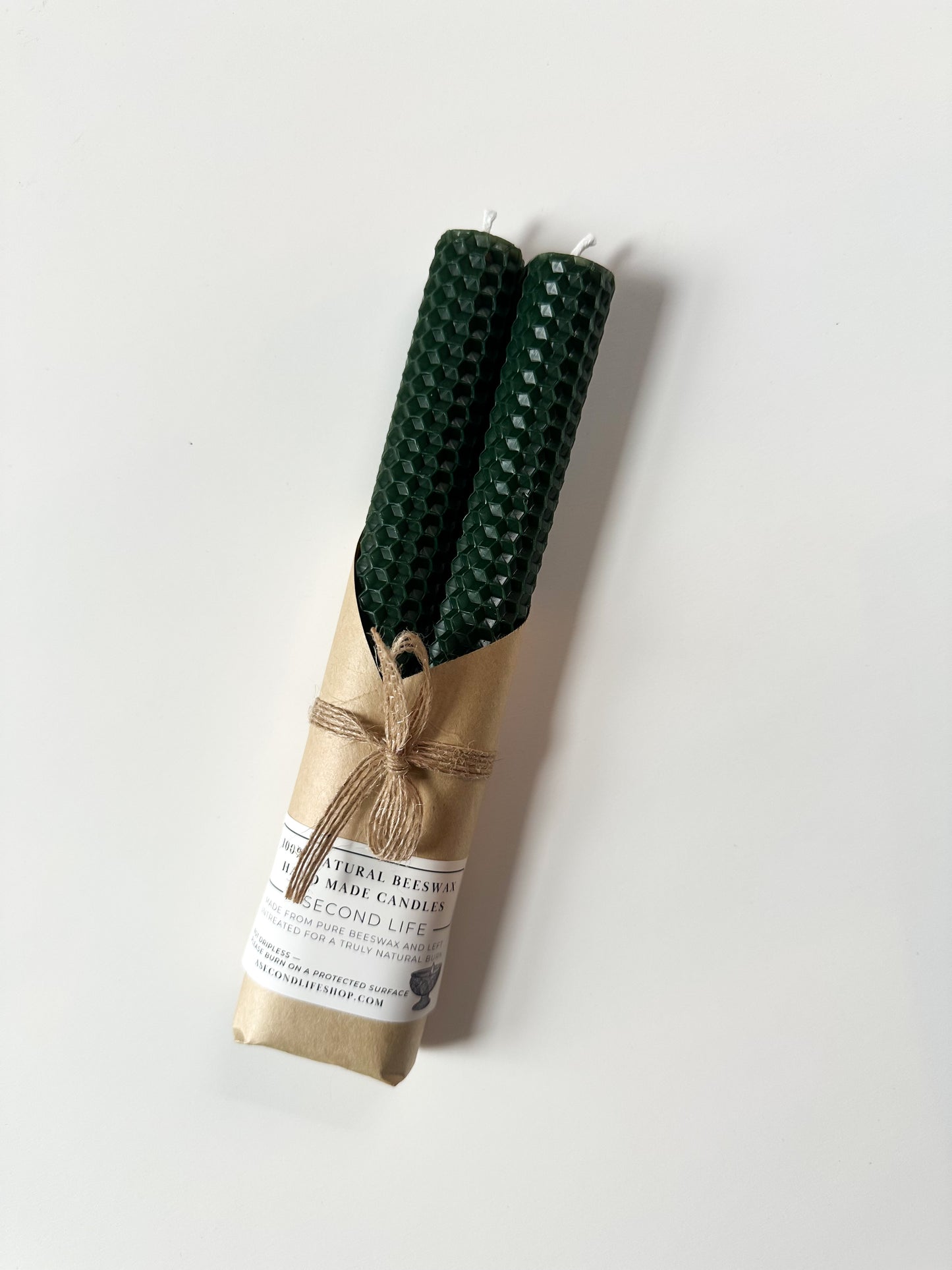 Two green candles wrapped in brown paper with a label on a white background