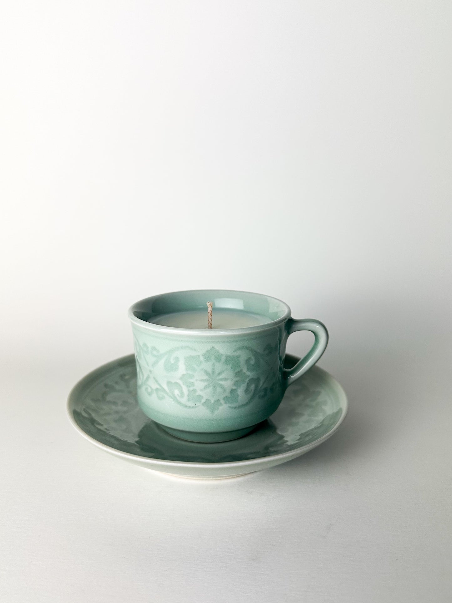Teal ceramic cup and saucer with a candle on a white background